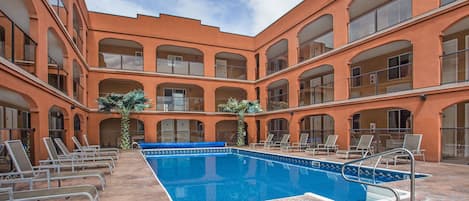 A pool area with lounge chairs and a clear blue pool, surrounded by a building with arched windows and balconies.