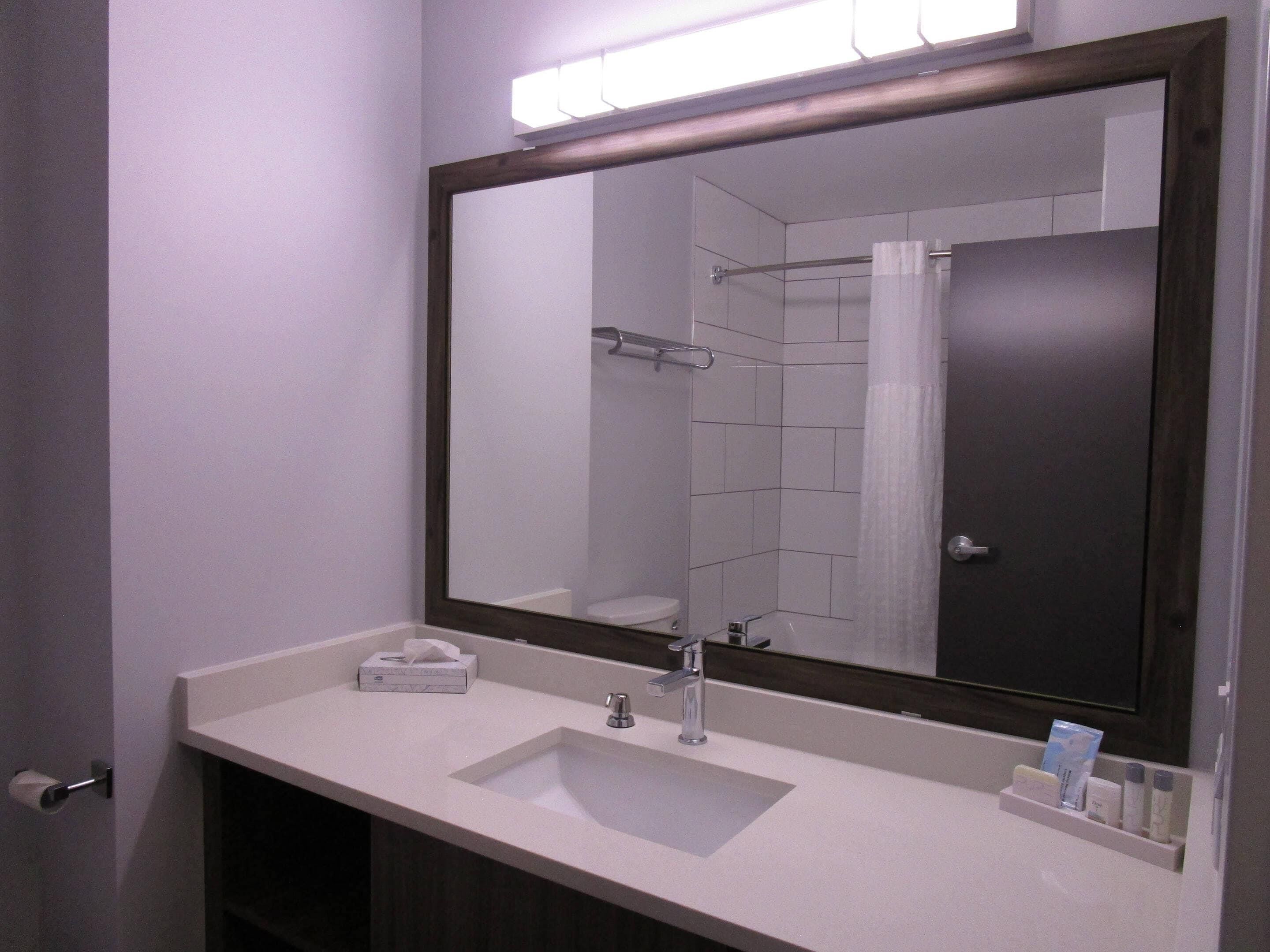 Un baño con un espejo grande, un lavabo y un dispensador de toallas.