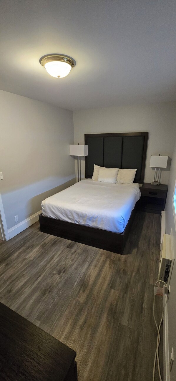 Una habitación de hotel moderna con una cama grande, dos mesitas de noche con lámparas, suelo de madera y una lámpara de techo.