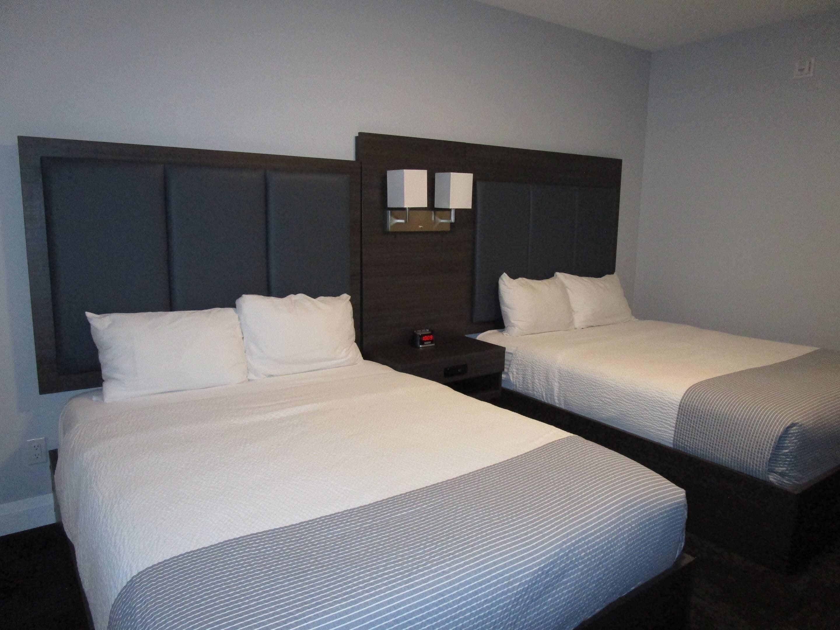 A hotel room with two single beds, a nightstand with a clock, and a mirror above the headboard.
