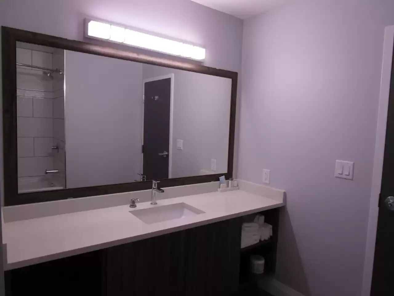 A bathroom with a white sink, dark cabinets, a large mirror, and a shower area.