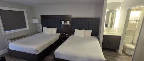 Habitación de hotel con dos camas, un ventanal grande, un baño con inodoro y lavabo, y un espejo.