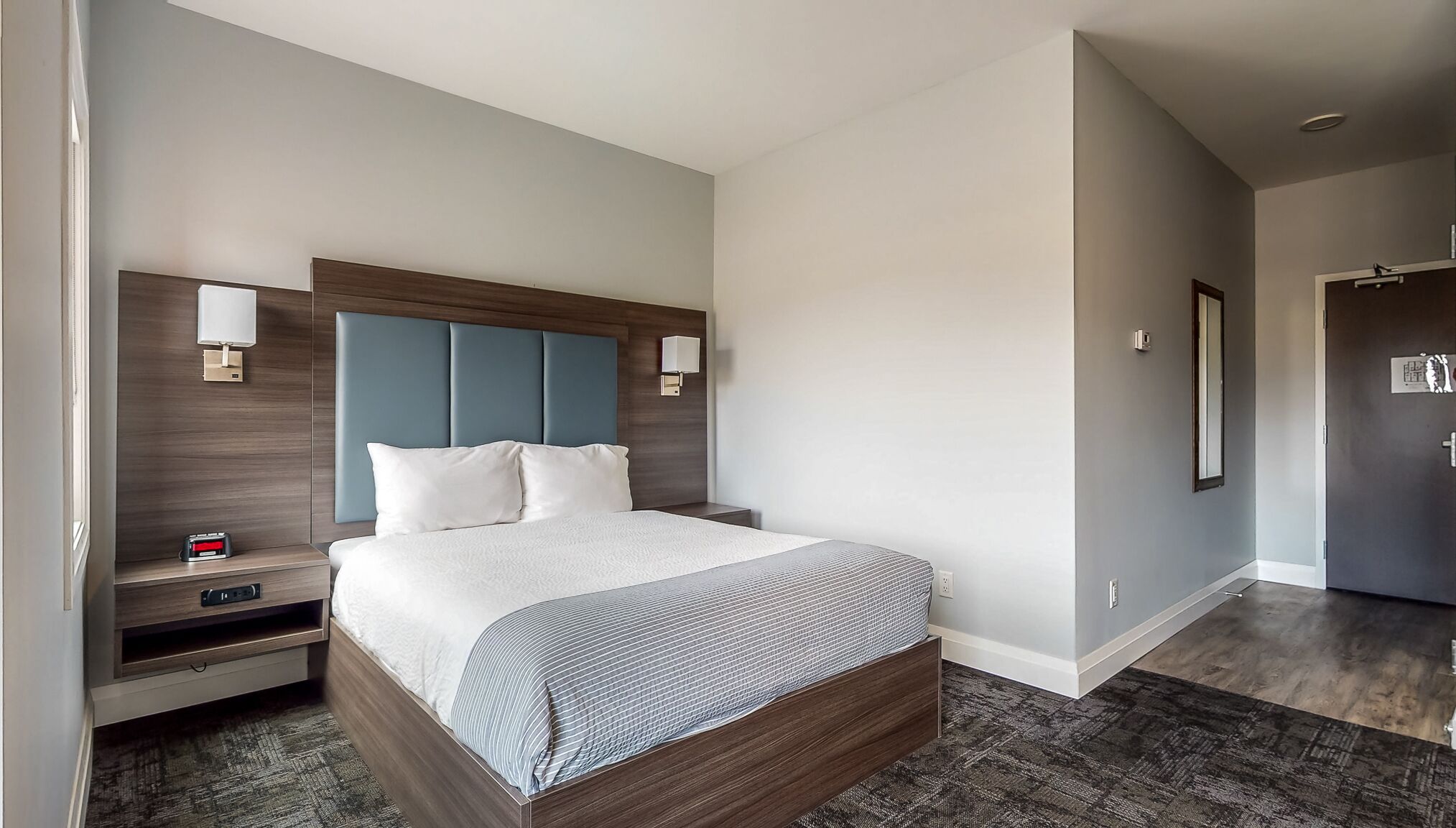 Une chambre d’hôtel moderne avec un grand lit, une tête de lit en bois, des tables de chevet et une petite table de nuit.