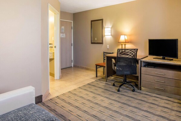 A hotel room with a desk, chair, TV, and a lamp.