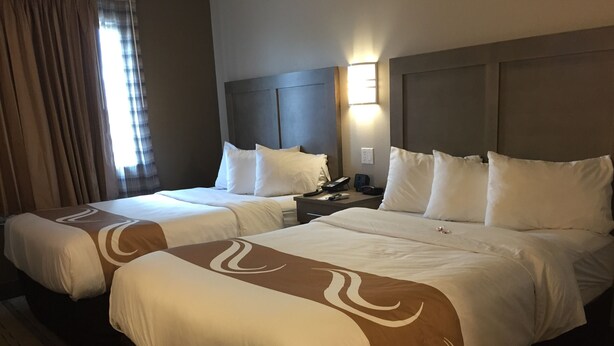 A hotel room with two beds, each with white bedding and a brown accent design. There is a nightstand with a phone and a lamp between the beds. - Quality Inn Moriarty (Moriarty)