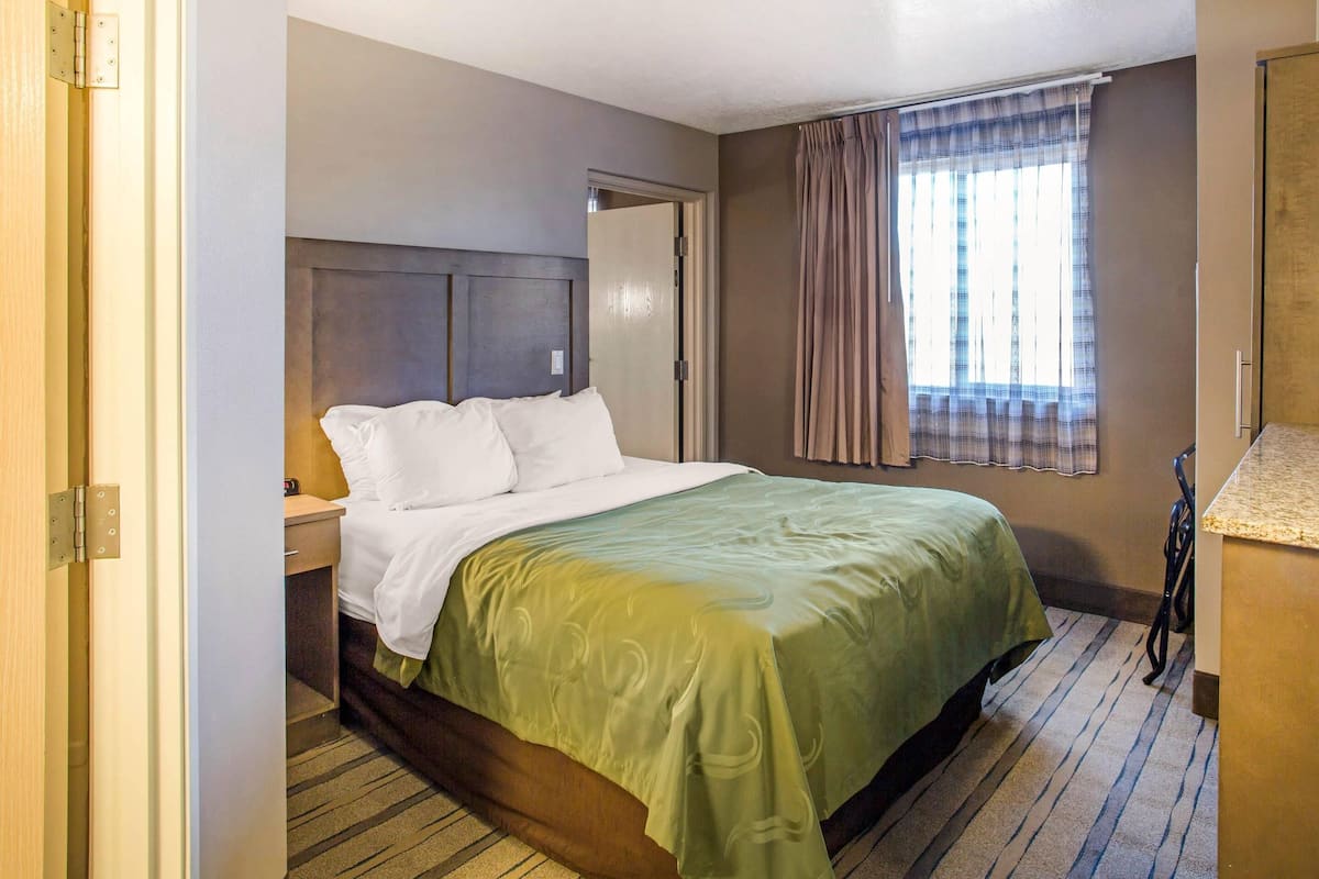 A hotel room with a bed, a nightstand, a window with curtains, and a door.