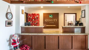 A hotel reception area with a wooden reception desk, a clock, and a Christmas-themed wall decoration. - Quality Inn Moriarty (Moriarty)