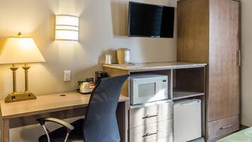 Quarto de hotel com escrivaninha, cadeira, micro-ondas, televisão e guarda-roupa.
