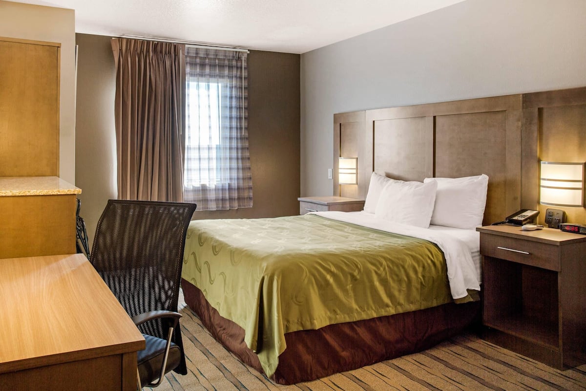 A hotel room with a bed, bedside table, lamp, and a chair.