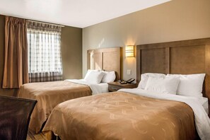 A hotel room with two beds, a nightstand, a lamp, and a window with curtains. - Quality Inn Moriarty (Moriarty)