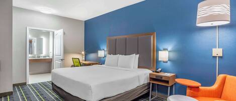 A hotel room with a large bed, a nightstand, a chair, and a lamp.