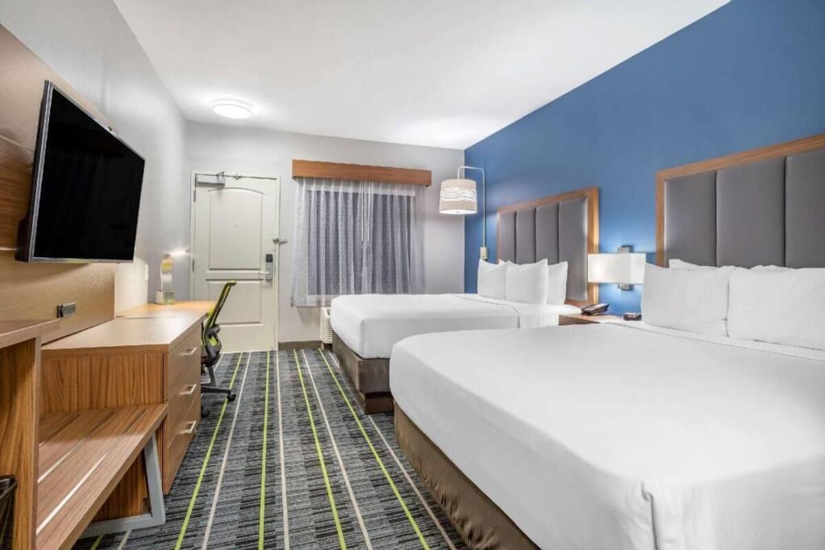 A hotel room with two beds, a desk, a television, and a window with curtains.