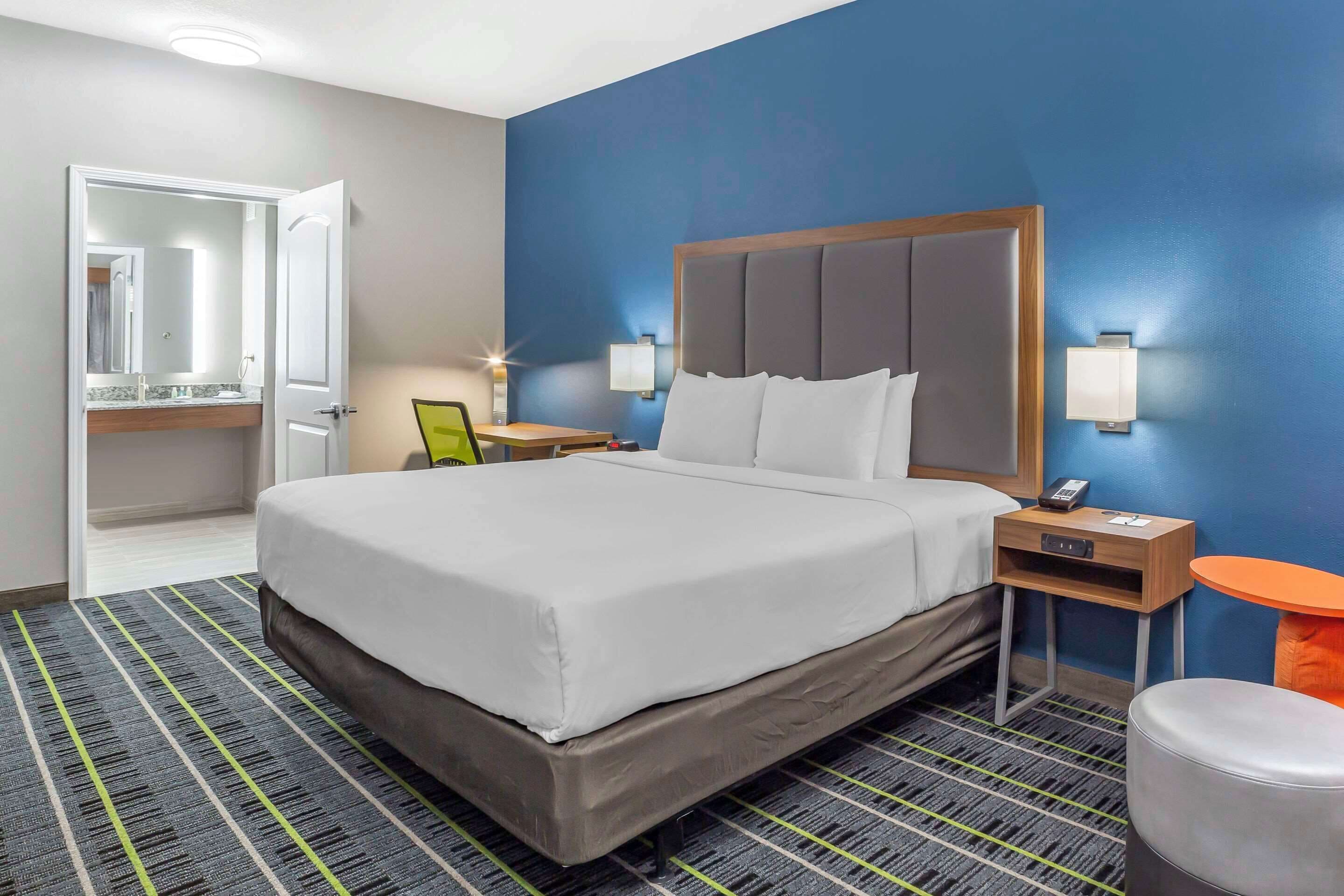 A hotel room with a large bed, a bedside table with a lamp, a small table, and a chair.