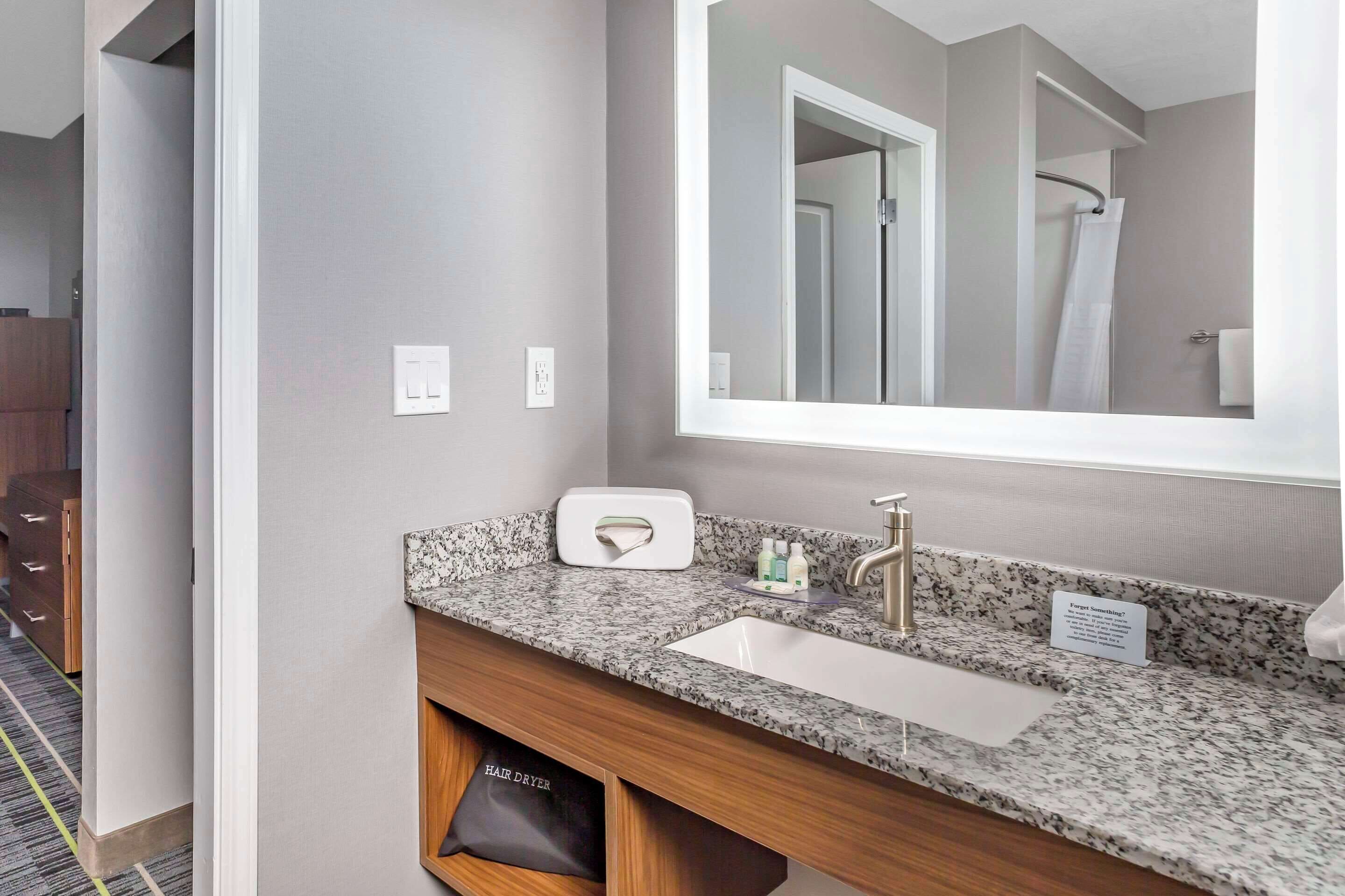 A modern bathroom with a granite countertop, a white sink, and a large mirror.