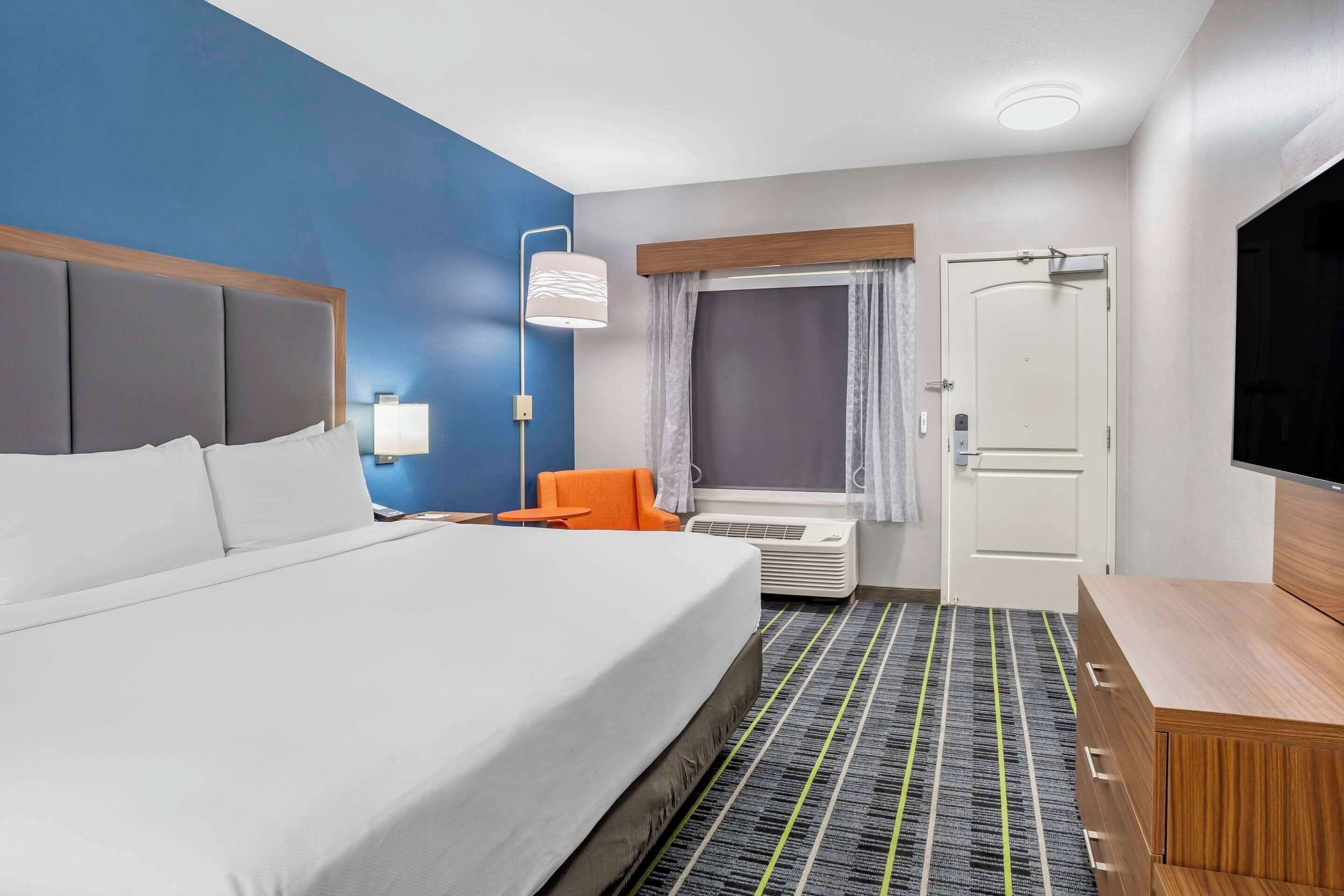 A hotel room with a large bed, an orange chair, a TV, and a desk with drawers.