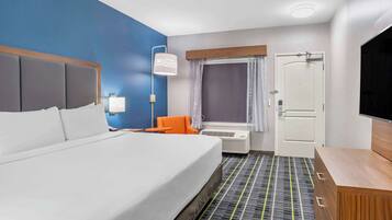 A hotel room with a large bed, an orange chair, a TV, and a desk with drawers.