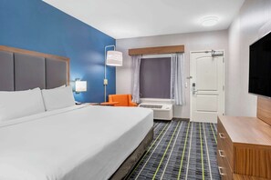 A hotel room with a large bed, an orange chair, a TV, and a desk with drawers.