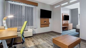 A hotel room with a wooden desk, a chair, a TV mounted on the wall, a small wooden cabinet, and a window with curtains. - Quality Inn & Suites Livermore Wine Country (Livermore)