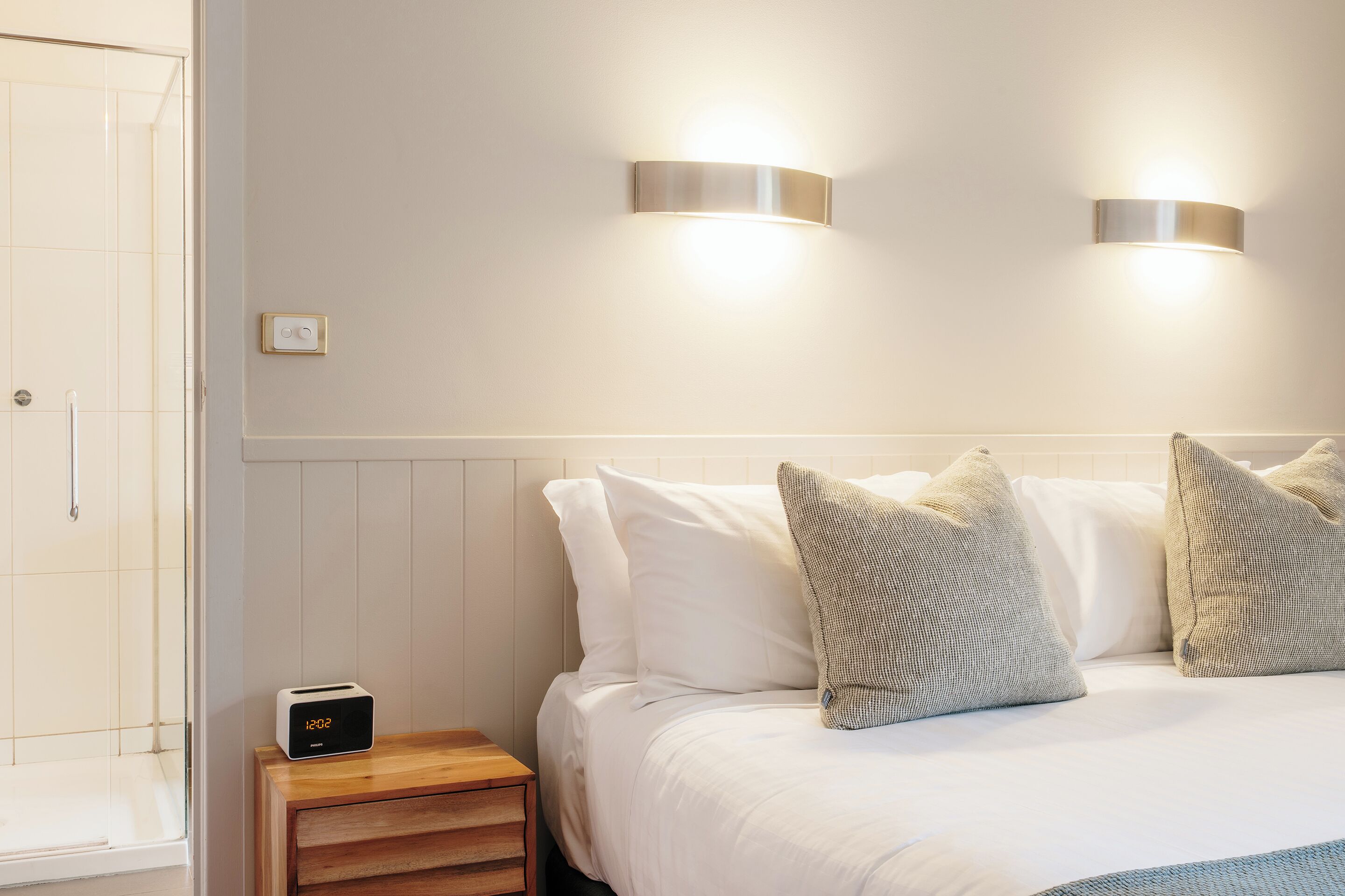 Hotelkamer met een bed, twee wandlampen, een nachtkastje met een klok en een douche.