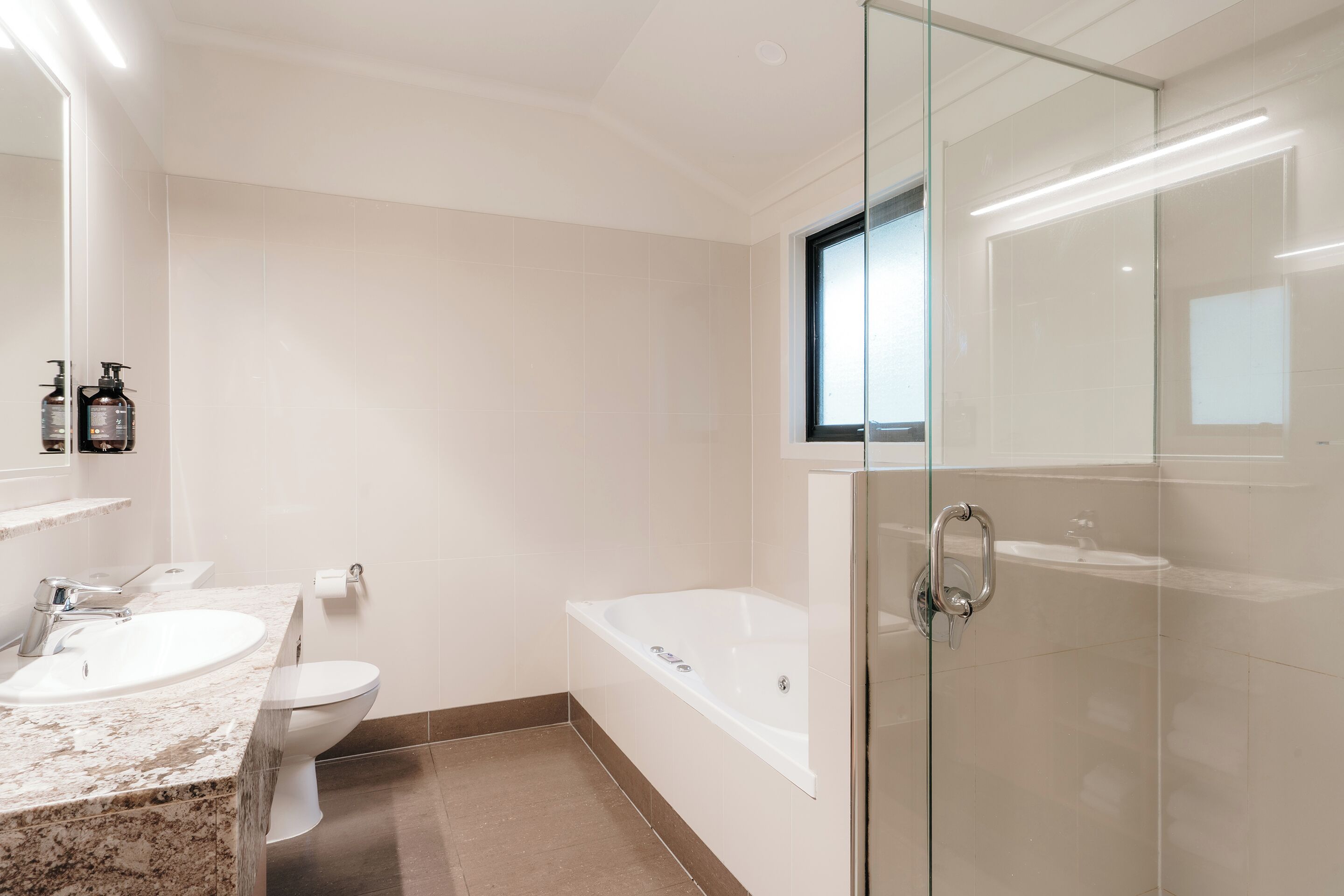 A modern bathroom with a glass-enclosed shower, a bathtub, and a marble sink.