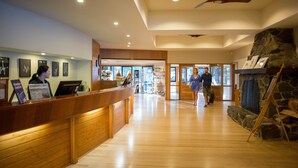 A reception area with a wooden counter, framed pictures on the wall, and a stone fireplace. - Freycinet Lodge (Coles Bay)
