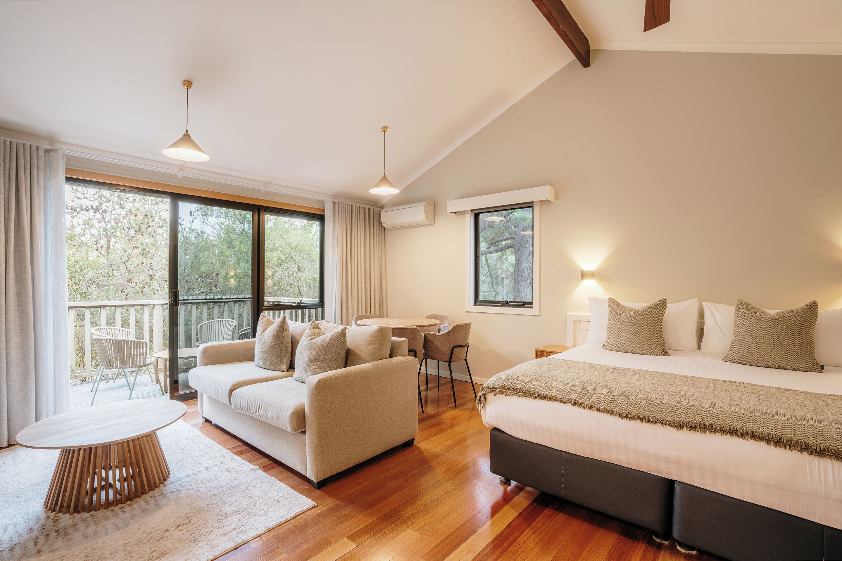 A modern bedroom with a large bed, a sofa, a dining table, and a balcony with chairs.