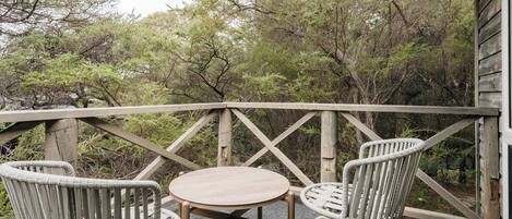 A wooden deck with a round table and two wicker chairs, surrounded by trees.