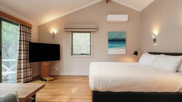 A bedroom with a bed, a TV, a window, and a painting.