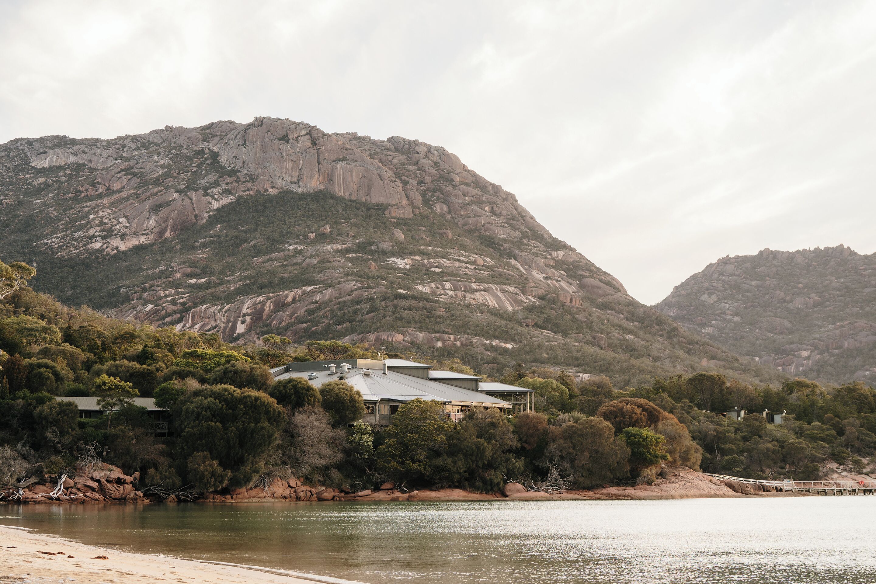 A house with a large roof, surrounded by trees and a mountain in the background.