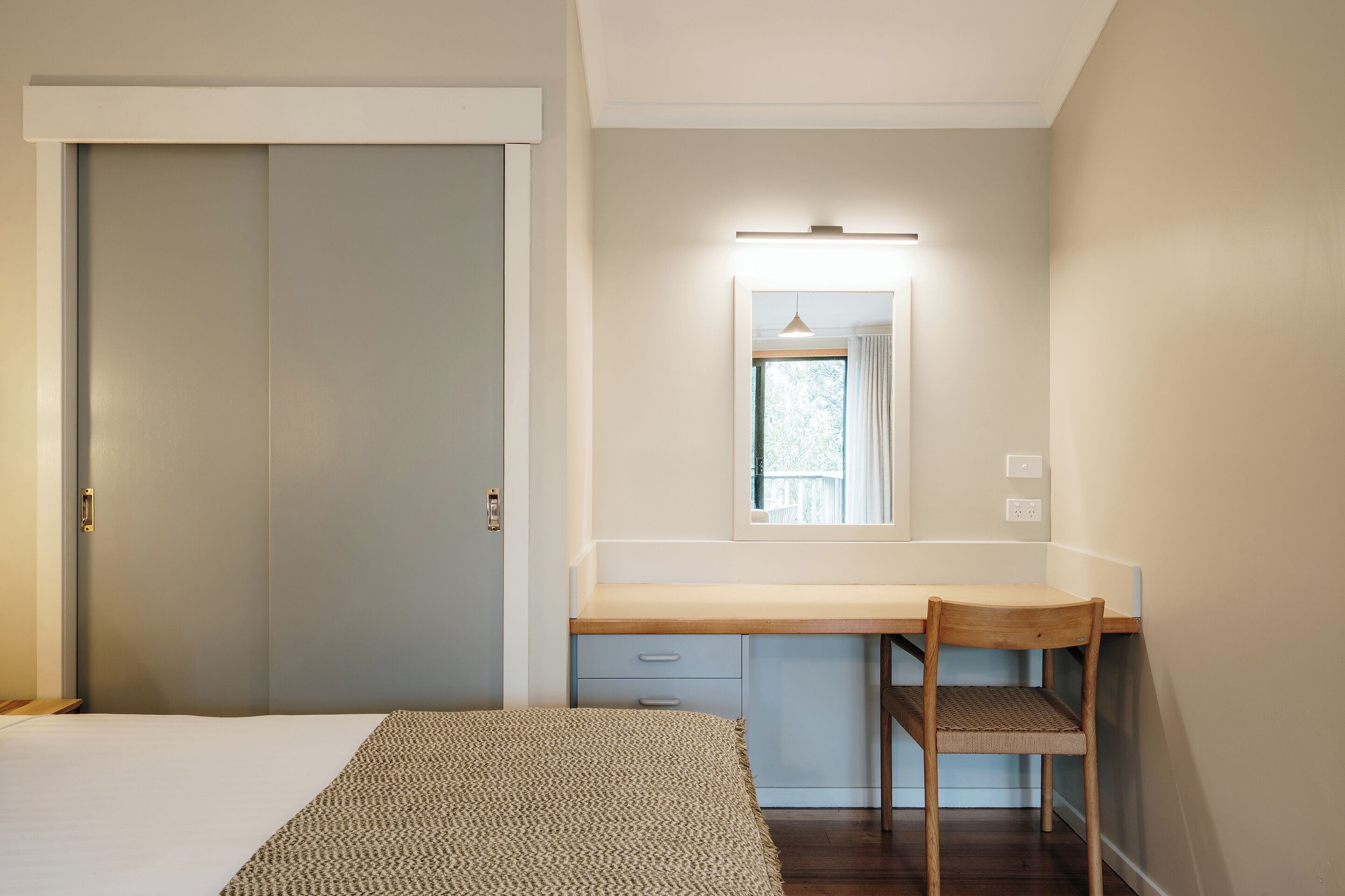 Ein Schlafzimmer mit Bett, Schreibtisch mit Stuhl, Fenster mit Blick und einer Tür.