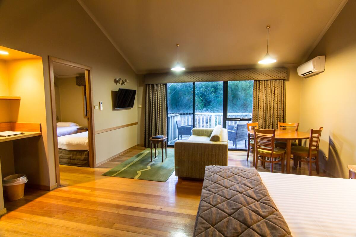 Habitación de hotel con cama, escritorio, silla, mesita, sofá, ventana con cortinas y aire acondicionado.