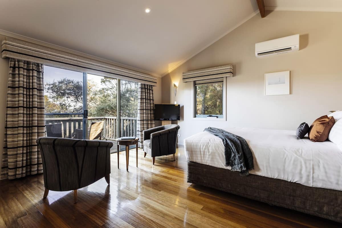 Un dormitorio con cama, televisión, balcón con cortinas y suelo de madera.