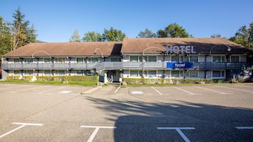 Un motel con un letrero que dice 'HOTEL' y 'Kyriad' en la fachada. Cuenta con un estacionamiento al frente.