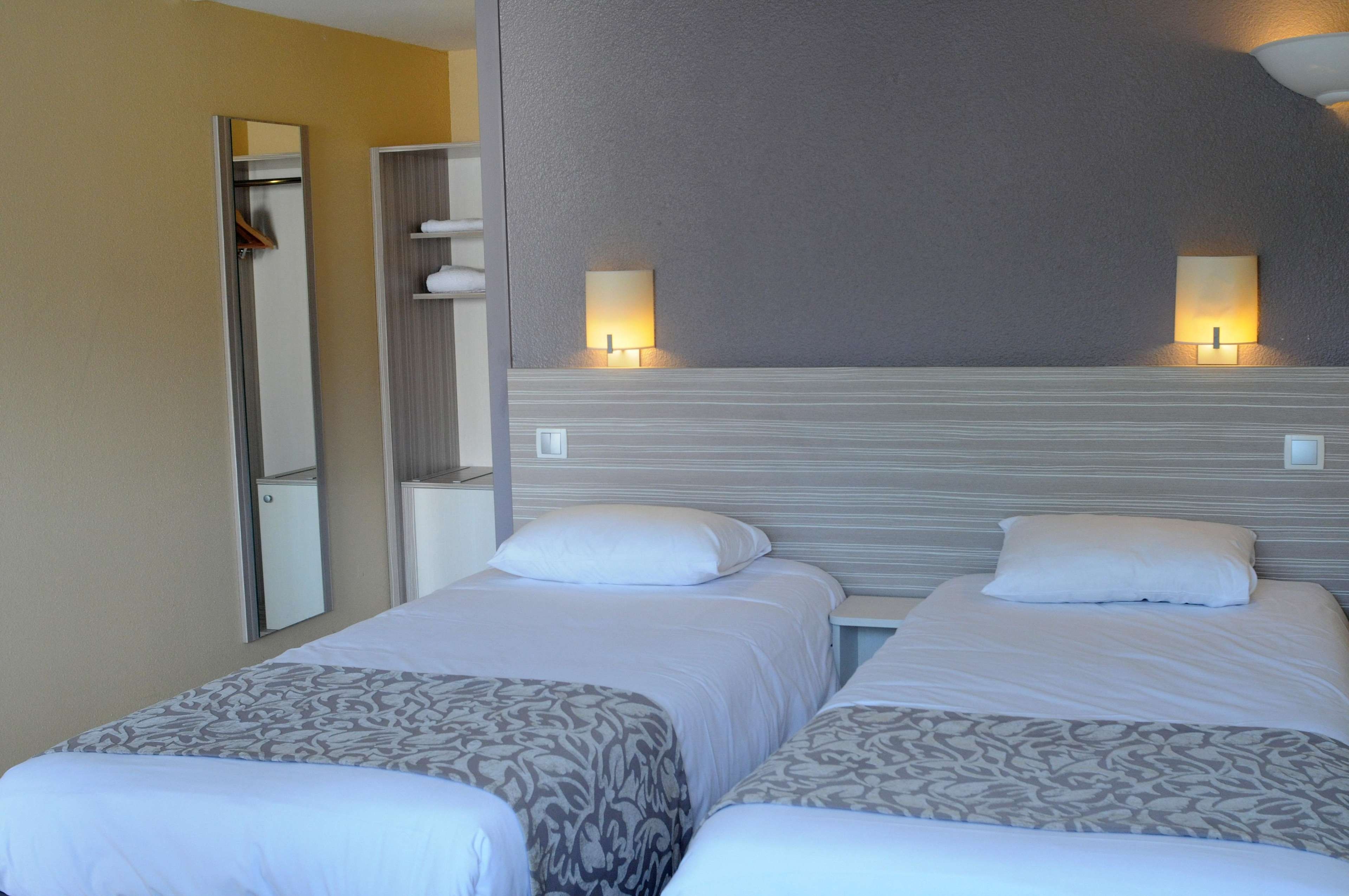 Een hotelkamer met twee bedden, een spiegel en twee wandlampen.
