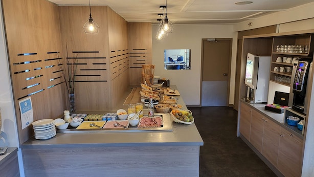 Een ontbijtbuffet met diverse gerechten, een koffieapparaat en een zithoek met stoelen.