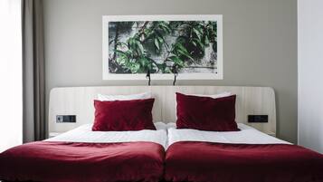 A hotel room with a bed, two red pillows, a white comforter, and a wall-mounted artwork of green leaves.