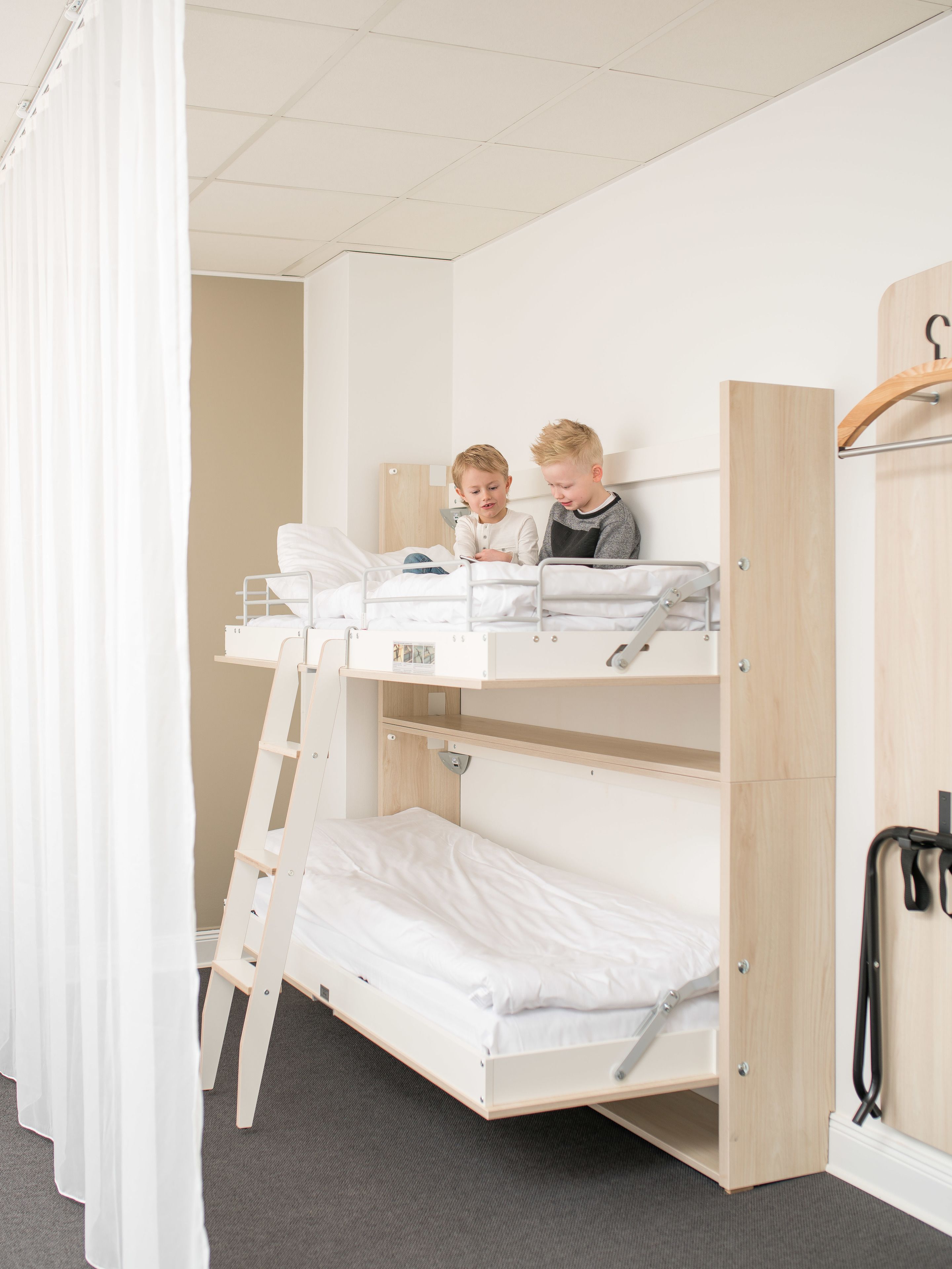 A bunk bed room with two children sitting on the top bunk.