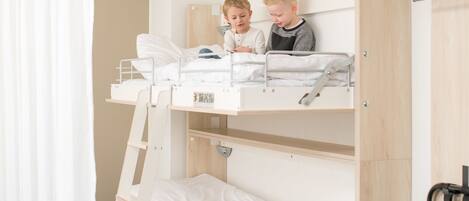A bunk bed room with two children sitting on the top bunk.