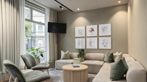 A modern living room with a sectional sofa, a round coffee table, and a flat-screen TV mounted on the wall. - Best Western Hotel Svava (Uppsala)