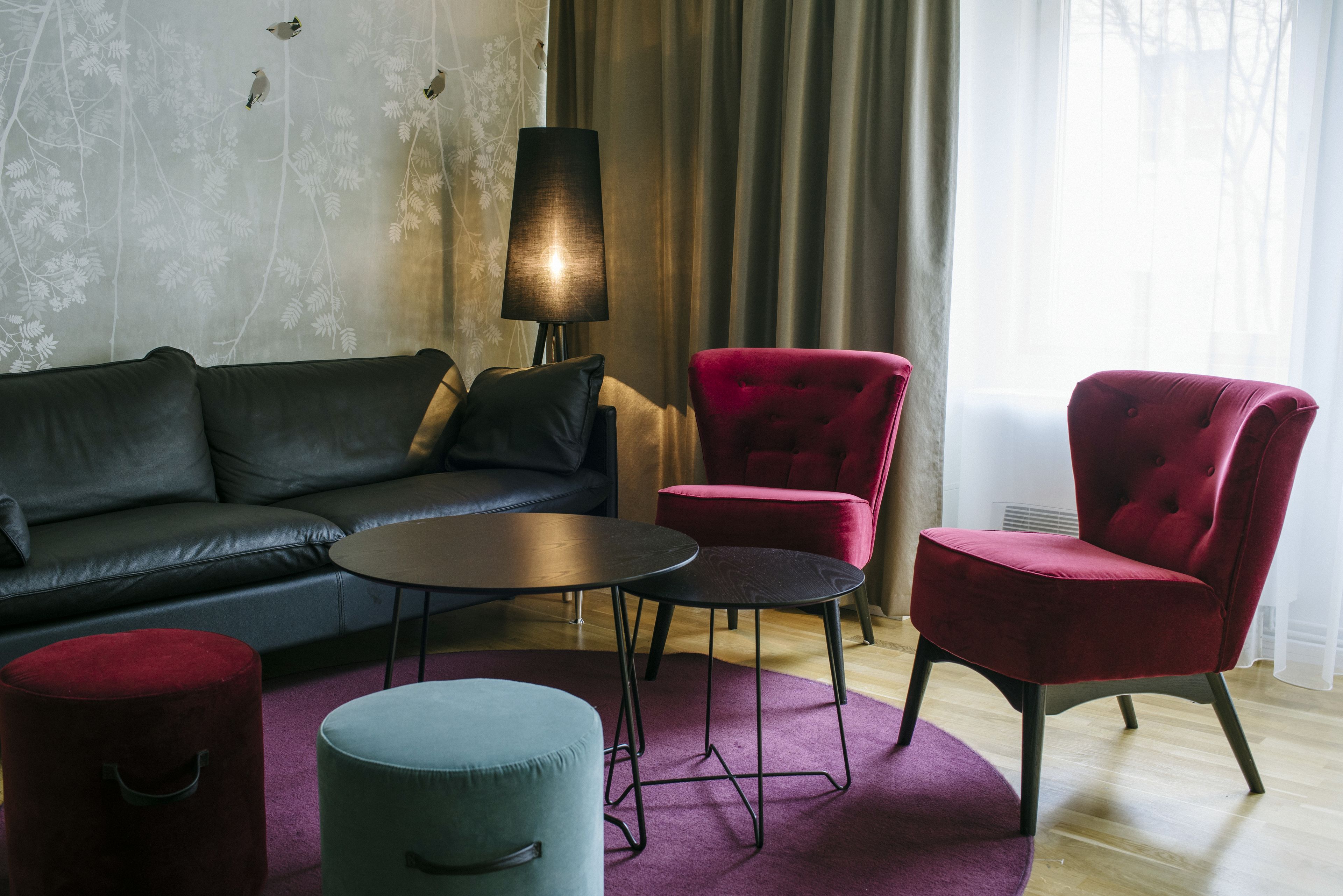 Un salon moderne avec un canapé en cuir foncé, un fauteuil en velours rouge, une table basse ronde et un petit pouf.