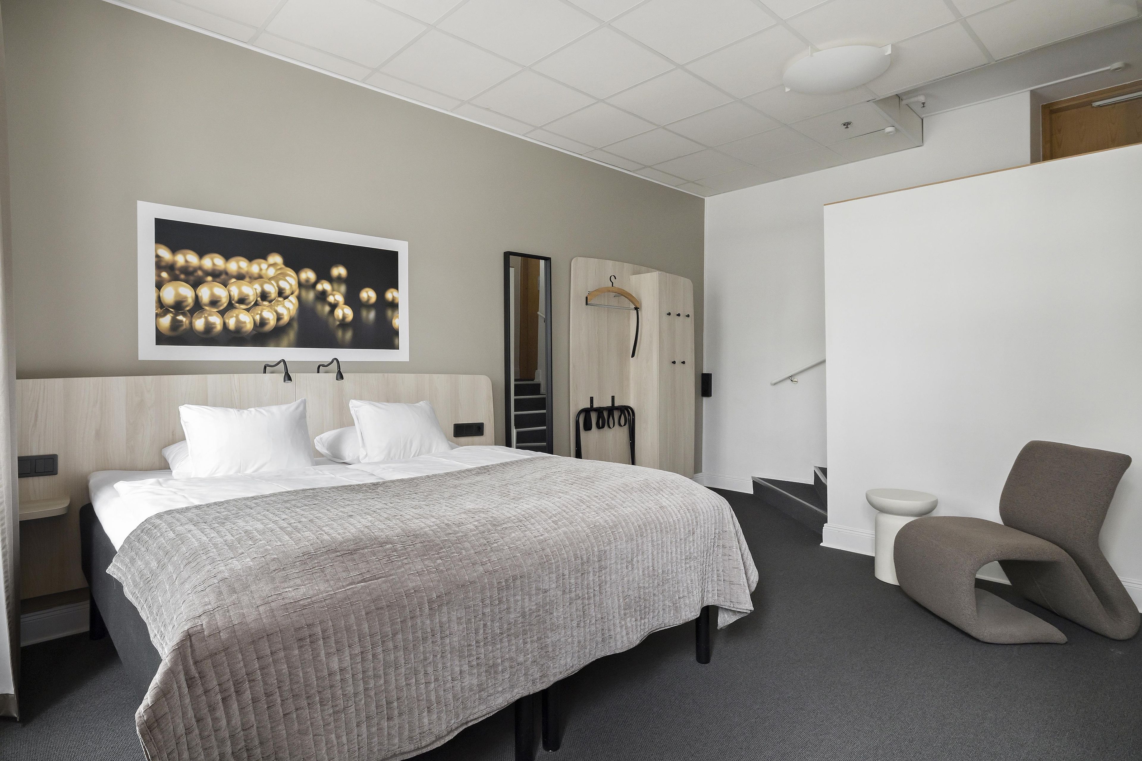 A hotel room with a bed, a chair, a wardrobe, and a mirror.