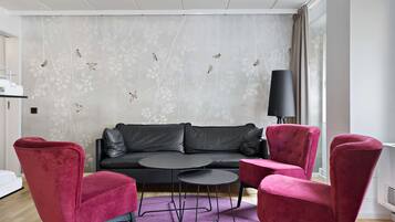 A modern living room with a black leather sofa, two red velvet chairs, a small black table, and a purple rug.