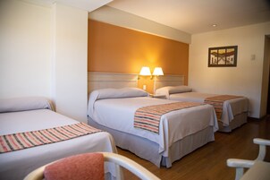 A hotel room with three single beds, each with a bedside table and lamp, and a large painting on the wall.