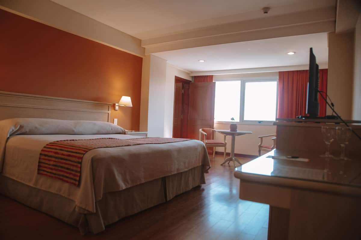 A hotel room with a bed, a desk with a computer, a chair, and a window with curtains.