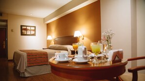 A hotel room with a bed, a bedside table with breakfast items, a lamp, and a painting on the wall. - Casa Real (Salta)