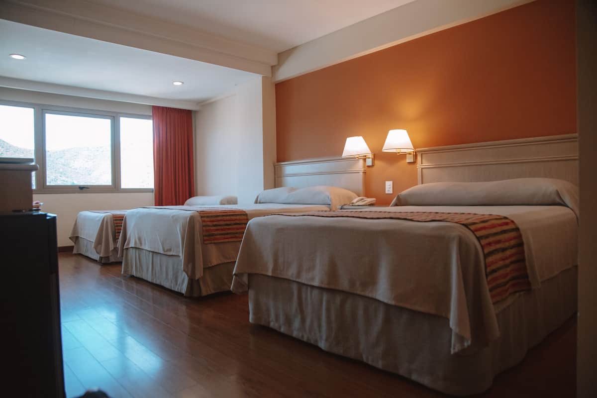 A hotel room with two beds, a window with a view, and a desk with a lamp.