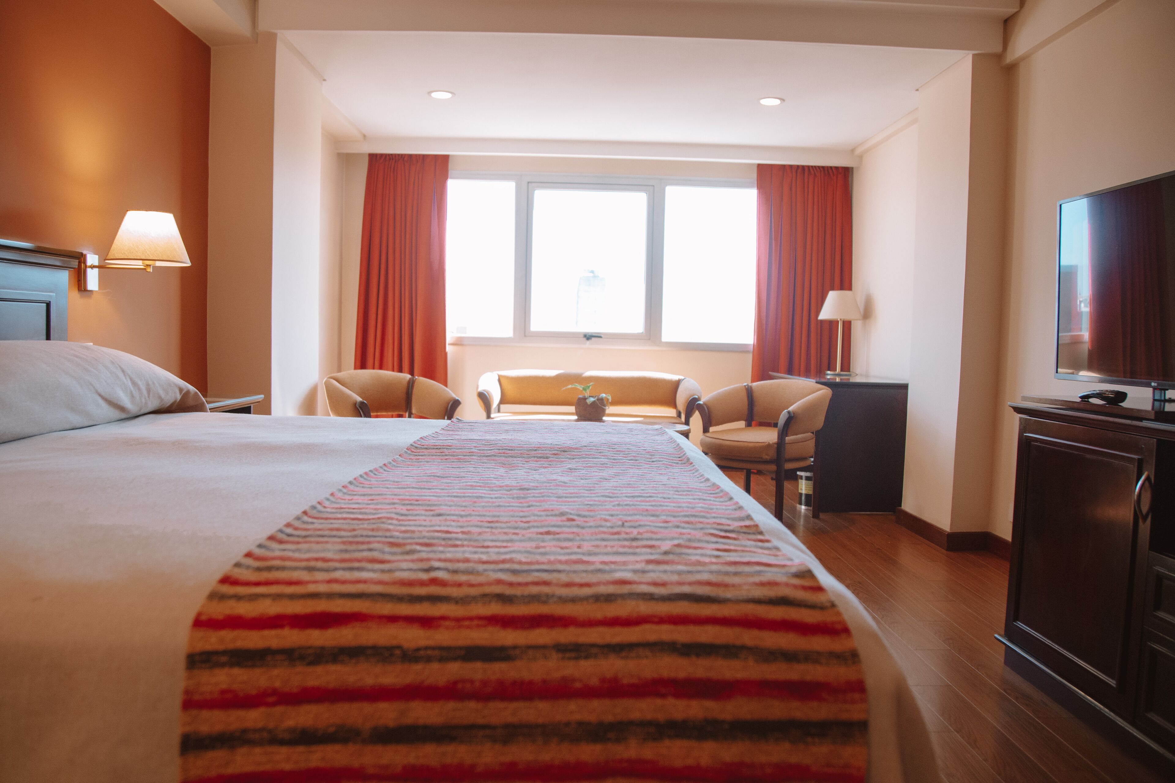Una habitación de hotel con una cama grande, un televisor, un escritorio y una ventana con cortinas.