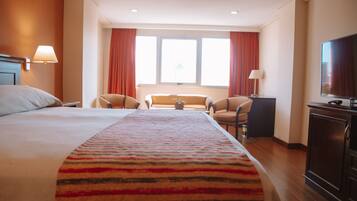 Una habitación de hotel con una cama grande, un televisor, un escritorio y una ventana con cortinas.