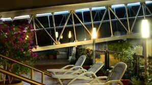 A covered outdoor seating area with lounge chairs and a railing, surrounded by potted plants and a metal structure overhead. - Casa Real (Salta)