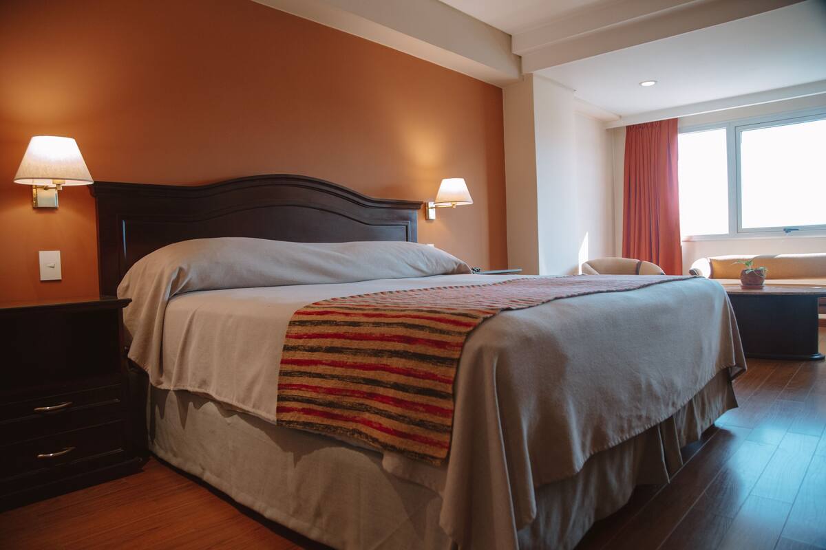 A neatly made bed with a striped blanket, two bedside lamps, and a window with curtains.